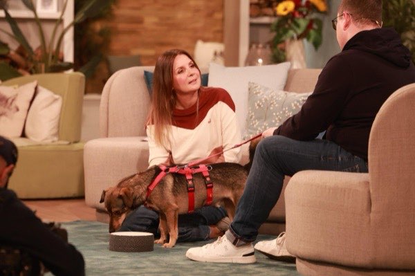 Moderatorin Simone Sombecki im Studio, davor ein kleiner Mischlingshund am roten Geschirr